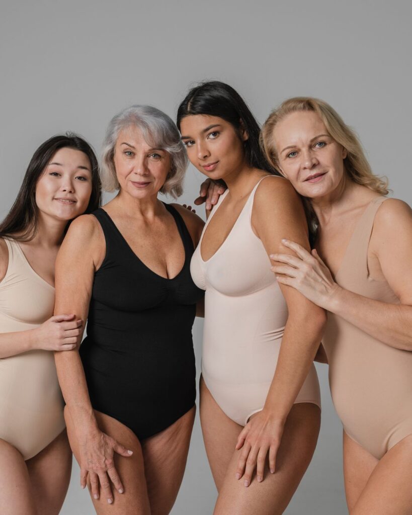 Four diverse women of different ages standing together in neutral-toned bodysuits, representing strength, unity, and body positivity