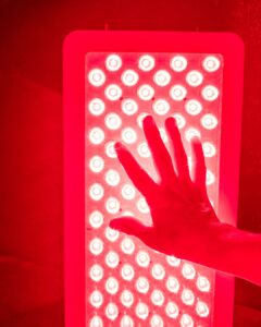 Hand placed in front of a red light therapy panel emitting bright LED light, representing the use of photobiomodulation for healing, recovery, and supportive cancer care.